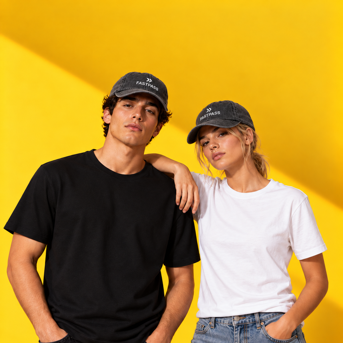 Zwei Models tragen anthrazitfarbene FASTPASS Vintage Caps mit weißer Stickerei vor gelbem Hintergrund.